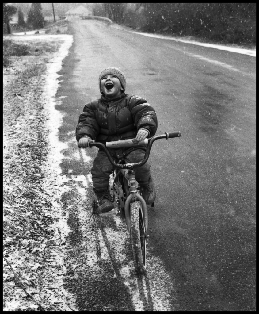 Boy riding a bike in the snow and laughing 